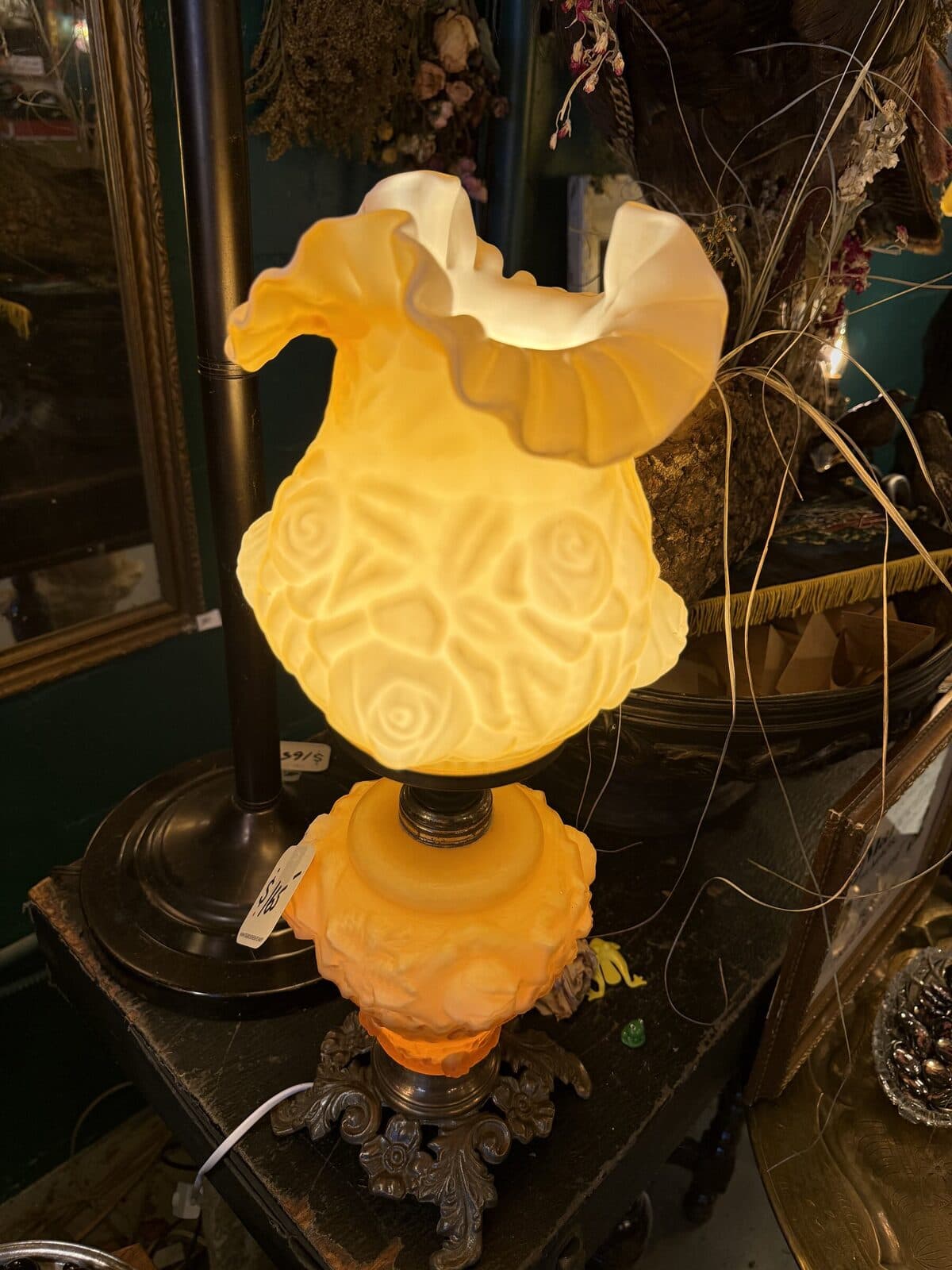 A vintage milk-glass globe lamp with painted floral pattern, glowing warm against a dark interior.